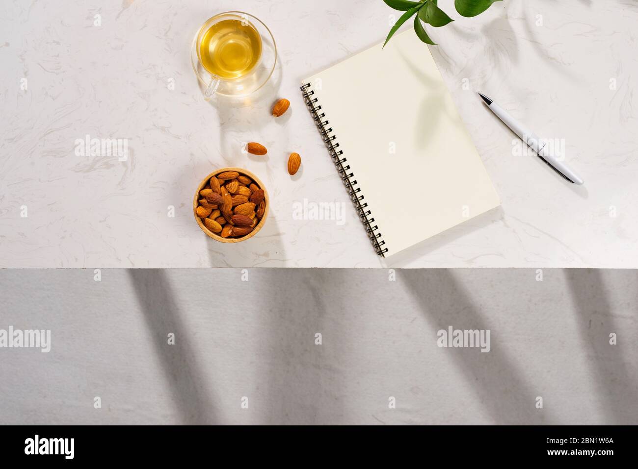 Plat de carnet, macaron à gâteaux, tasse de thé et feuilles sur table blanche Banque D'Images