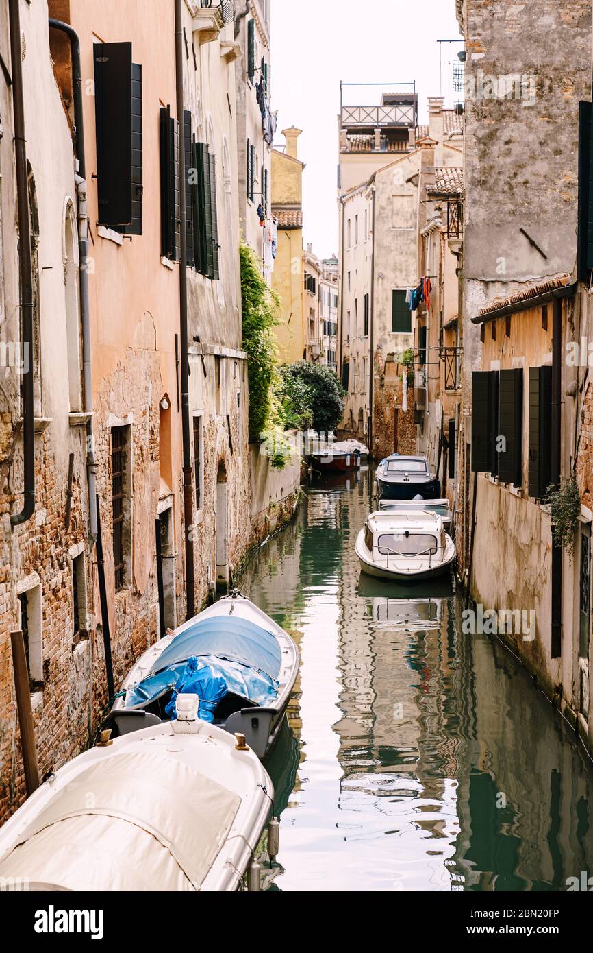 Bateaux amarrés aux murs des maisons dans l'eau de Venise. Étroit canal déserté entre les maisons, eau de mer azur au pied de la maison. Banque D'Images