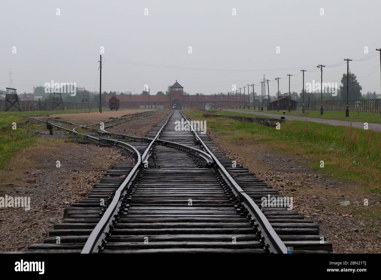 Musée Mémorial de l'Holocauste d'Auschwitz - vue de l'intérieur du camp le long des voies ferrées avec le portier d'Auschwitz II-Birkenau à distance, par une journée de dépassement Banque D'Images