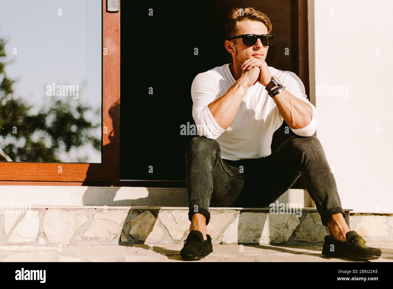 portrait d'un homme brutal et beau dans des lunettes de soleil et regarder à l'extérieur à la maison. Homme élégant portant décontracté. La beauté, la mode pour hommes. Optique pour hommes. Banque D'Images