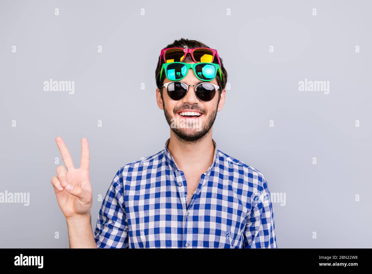 Cool ! Jeune joueur brunette barbu homme dans trois paires de verres colorés et de damier décontracté est dupe autour, pose et montre v Banque D'Images