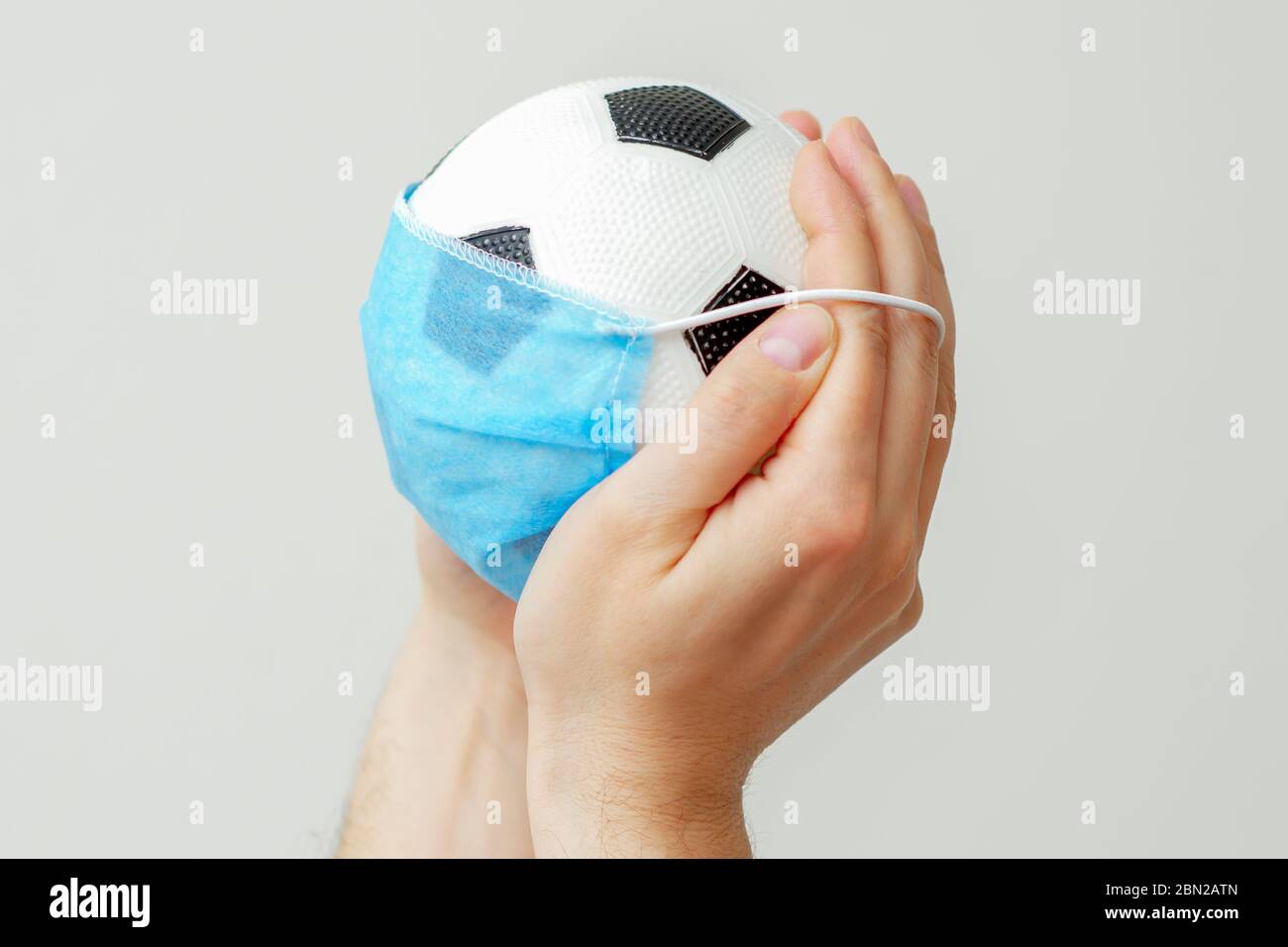 Gros plan du ballon de football avec un masque médical dans les mains de  l'homme sur un fond clair. Annulation d'événements sportifs Photo Stock -  Alamy