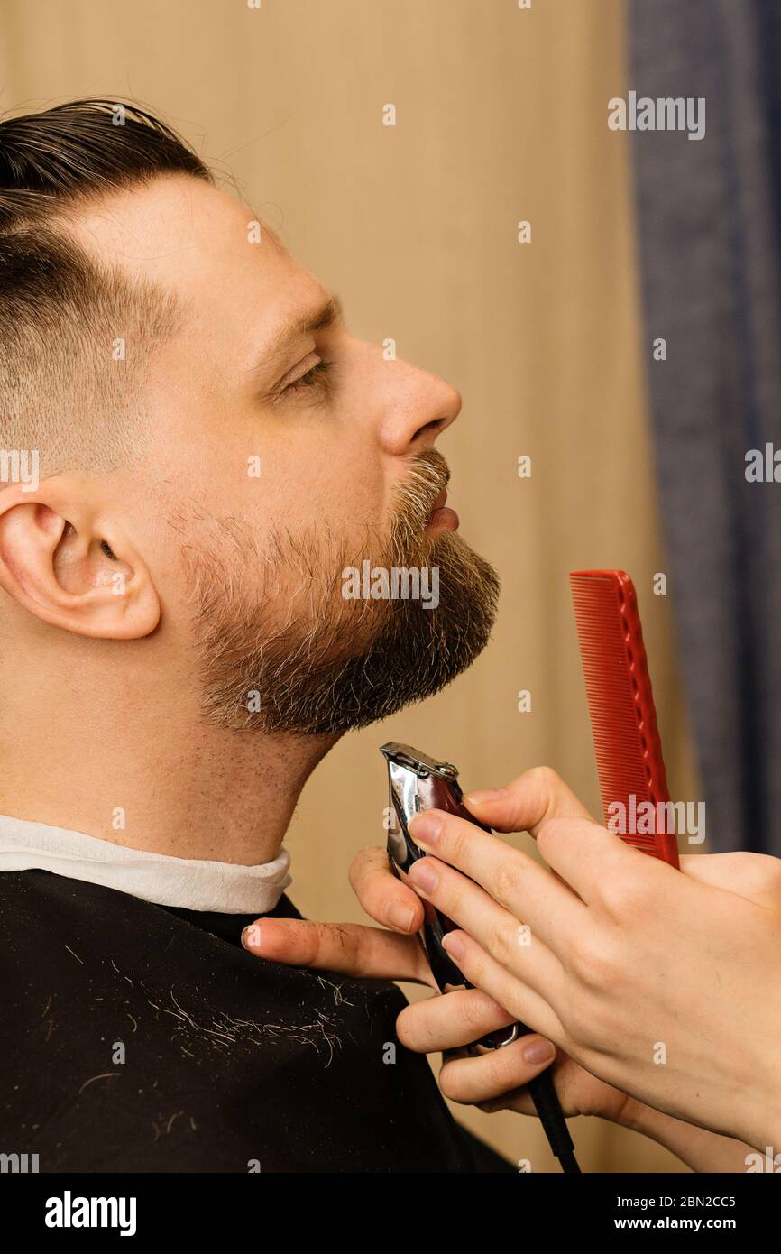 Barbier tailler la barbe d'un client masculin avec un rasoir électrique  dans un salon de coiffure. Homme avec barbe et moustache se raser les  cheveux avec tondeuse et sabot. Gros plan Photo