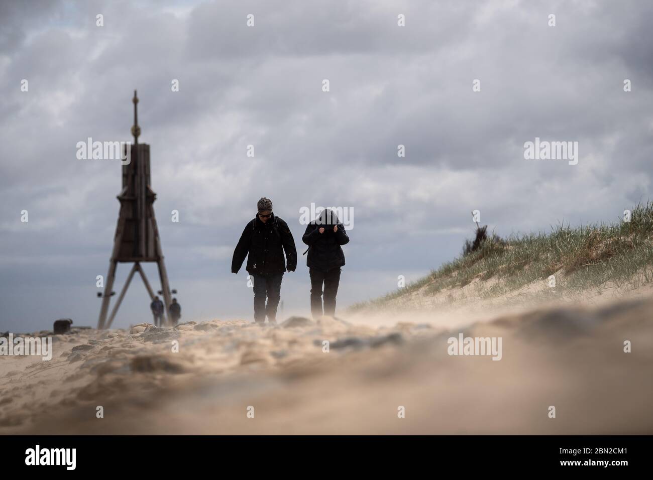 12 mai 2020, Basse-Saxe, Cuxhaven: Les marcheurs tiennent à leur capot à cause du vent en marchant sur la plage. Le tourisme en mer du Nord en Basse-Saxe est à nouveau en marche. Depuis lundi, les appartements de vacances ainsi que les sites de camping peuvent de nouveau être occupés à 50 pour cent d'occupation, sous réserve de conditions. Photo: Sina Schuldt/dpa Banque D'Images