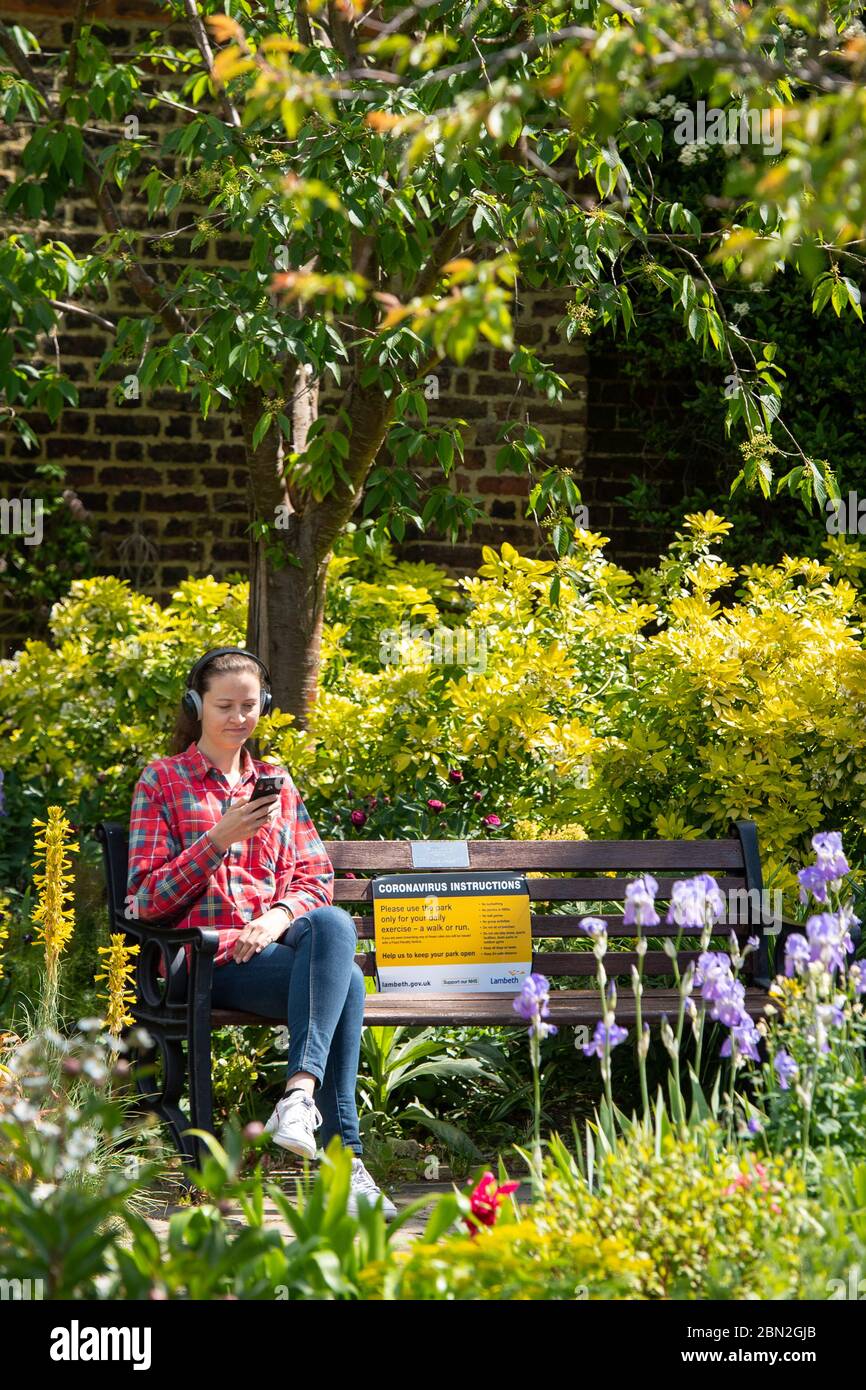 Une femme est assise à côté d'une pancarte portant des instructions sur le coronavirus alors qu'elle profite du soleil sur un banc de parc à Brockwell Park, dans le sud de Londres, après l'annonce de plans pour faire sortir le pays de son isolement. Banque D'Images