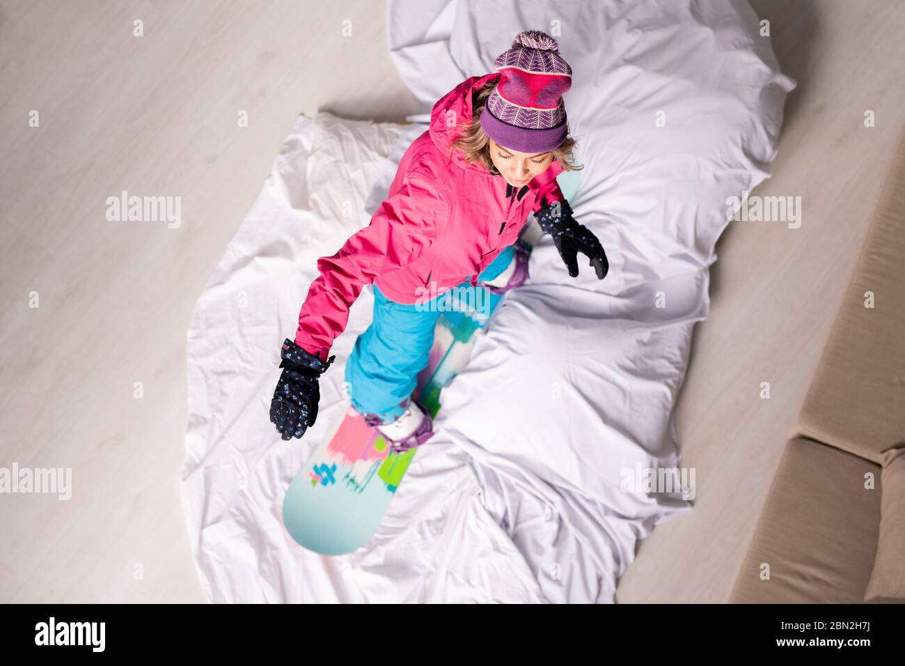 Vue au-dessus de la femme en vêtements chauds debout sur le snowboard à la maison avec couette blanche sur le sol comme il est neige, concept de période d'isolement Banque D'Images