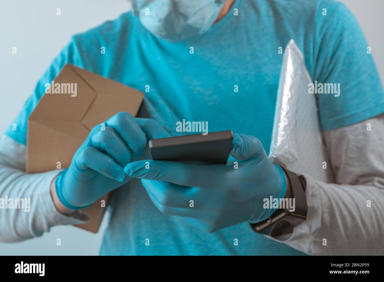 Homme de livraison avec des vêtements de protection utilisant un smartphone avec des gants de protection pendant une pandémie d'infection virale, foyer sélectif Banque D'Images