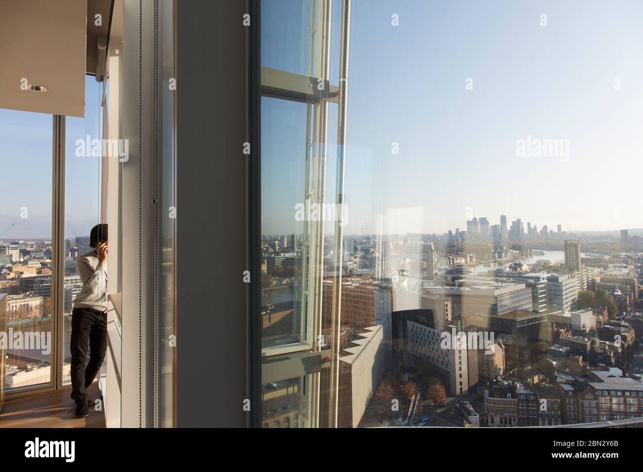 Homme d'affaires parlant sur un smartphone à la fenêtre de bureau urbaine Banque D'Images