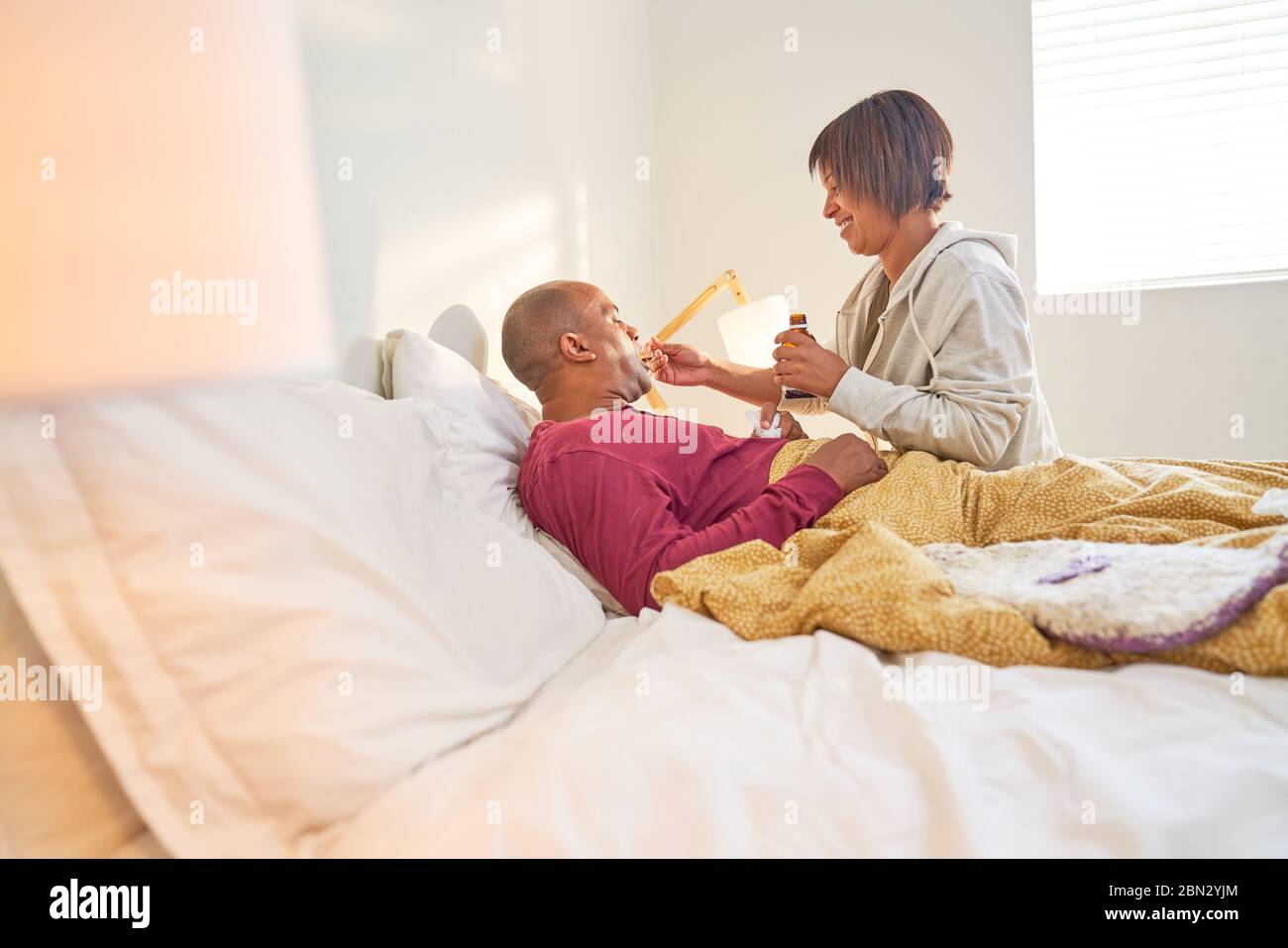 Femme affectueuse donnant du sirop contre la toux à un mari malade au lit Banque D'Images