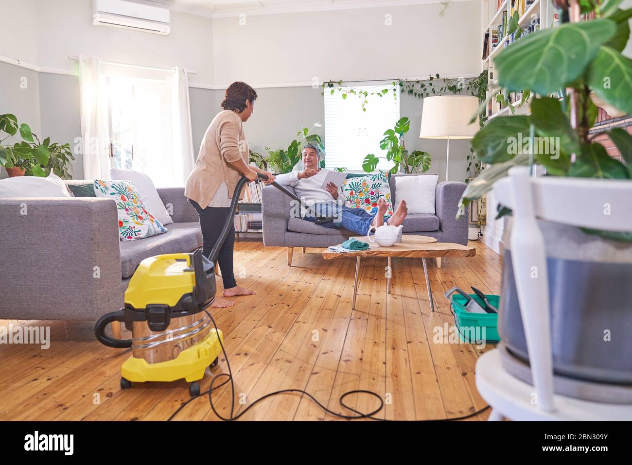 Femme passant l'aspirateur et parlant avec son mari dans le salon Banque D'Images