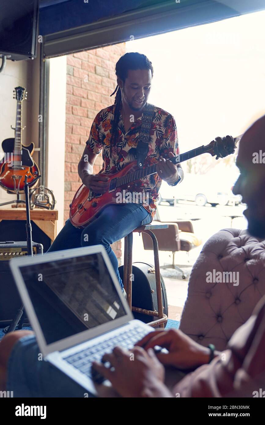 Musiciens de sexe masculin avec ordinateur portable et guitare pratiquant en studio d'enregistrement Banque D'Images