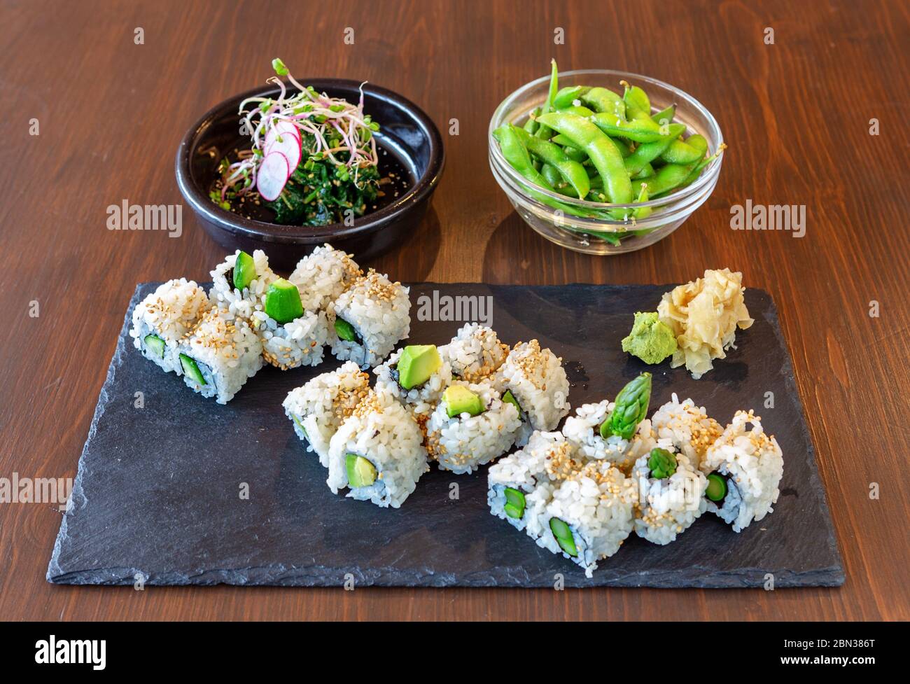 Sushi japonais avec avocat, riz, spécialités de mer sur pierre noire, sur fond marron. Assiettes avec salade et haricots verts. Banque D'Images