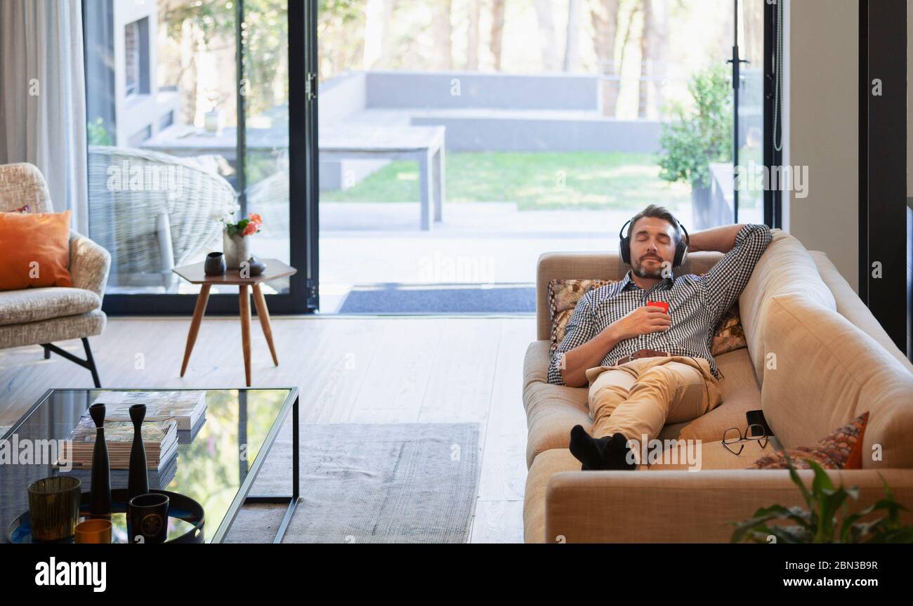 Homme se détendant sur le canapé du salon, en écoutant de la musique avec des écouteurs et un lecteur mp3 Banque D'Images