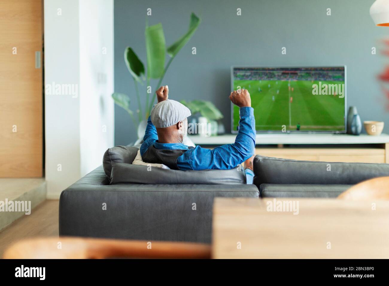 Un homme enthousiaste qui applaudisse, regarde un match de football à la télévision dans le salon Banque D'Images
