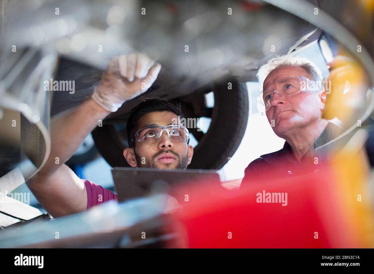 Mécanique masculine travaillant sous voiture dans l'atelier de réparation automobile Banque D'Images