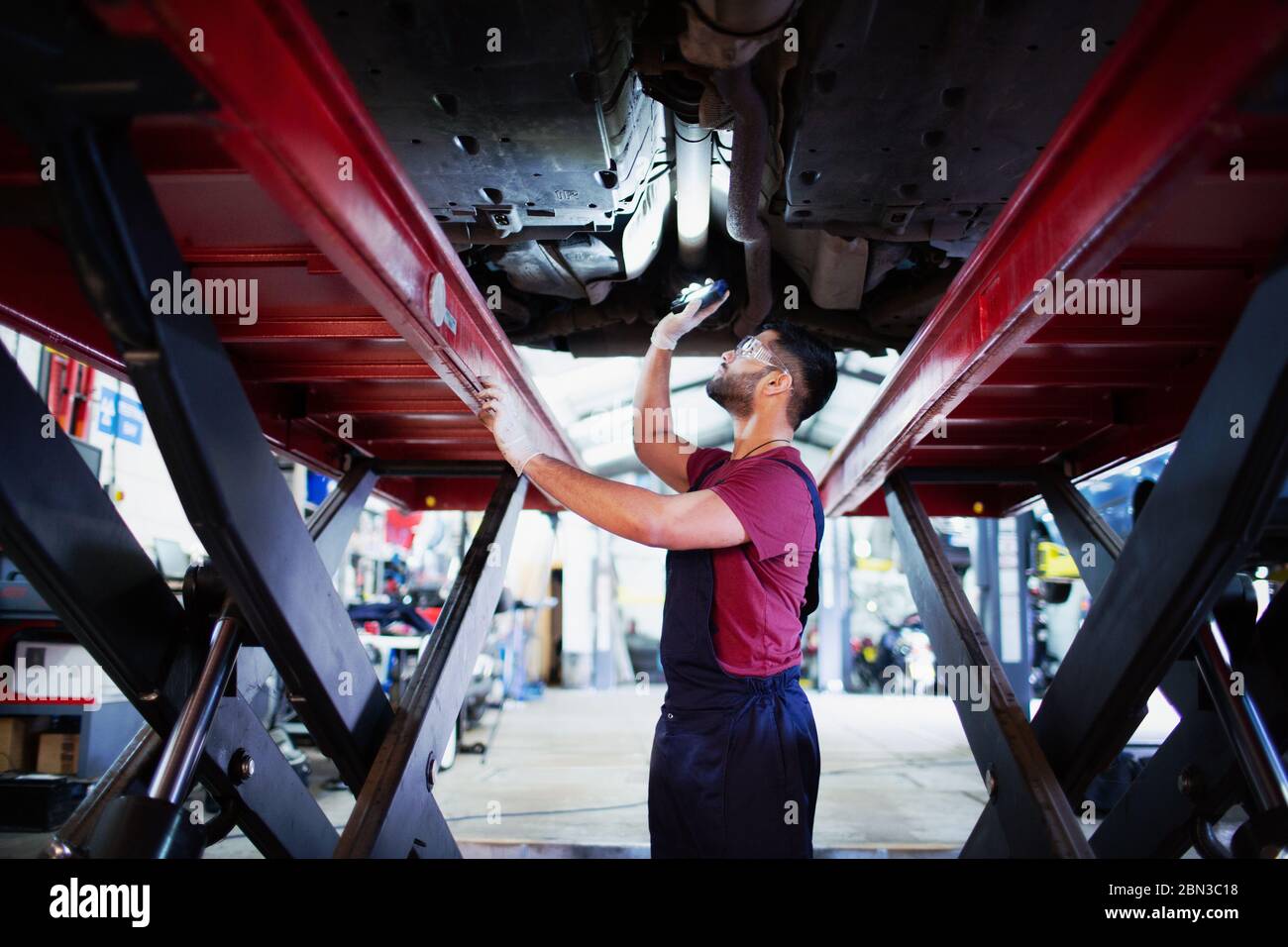 Mécanicien de sexe masculin avec lampe de poche sous la voiture dans un atelier de réparation automobile Banque D'Images