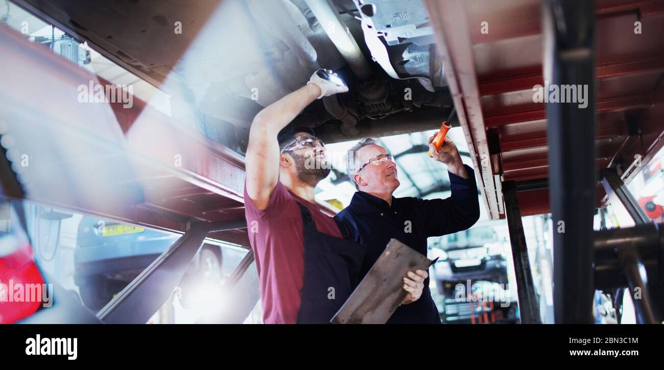 Mécanique masculine avec lampes de poche travaillant sous voiture dans l'atelier de réparation automobile Banque D'Images