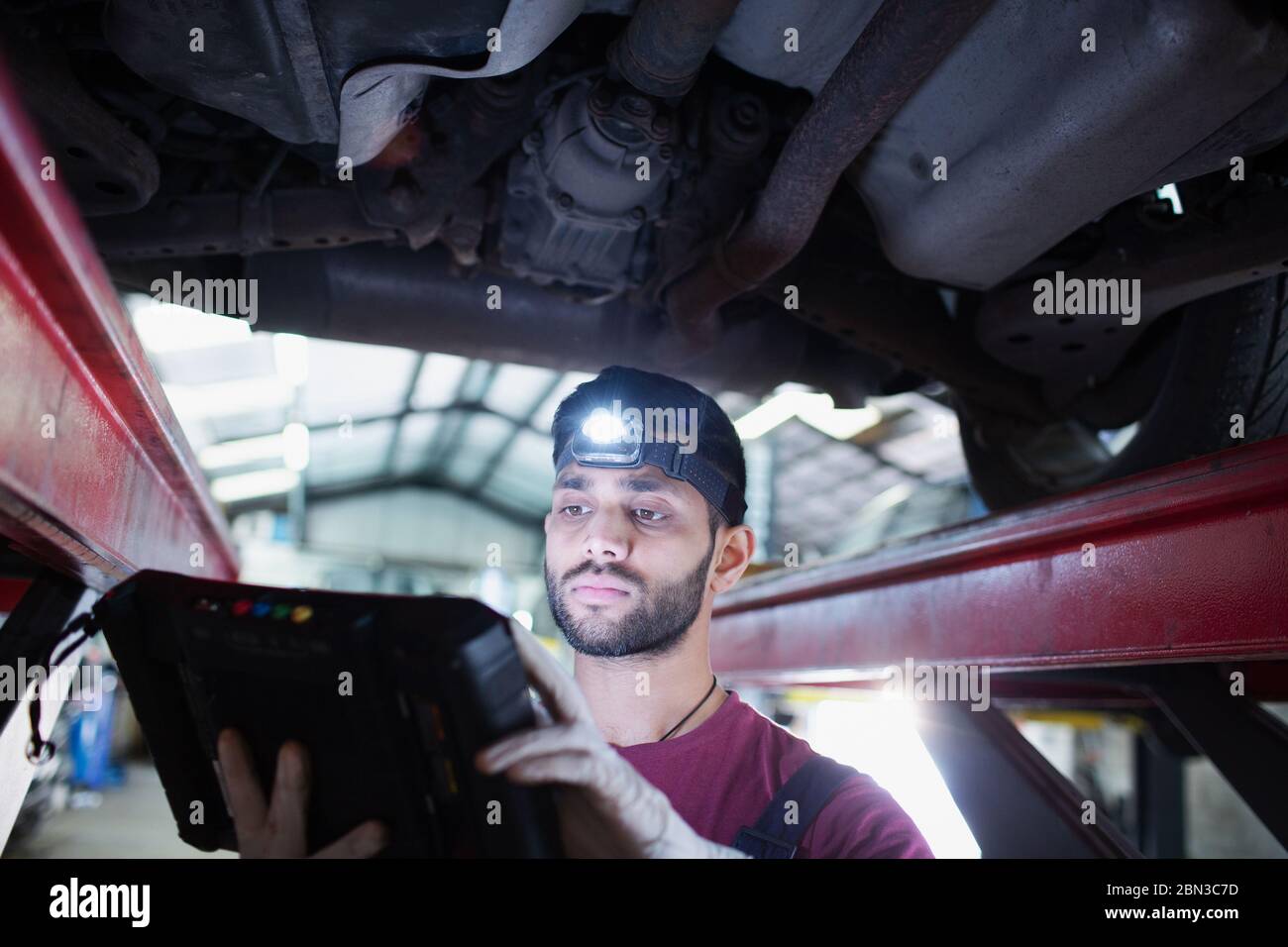 Mécanicien de sexe masculin avec projecteur et équipement de diagnostic travaillant sous voiture dans un atelier de réparation automobile Banque D'Images