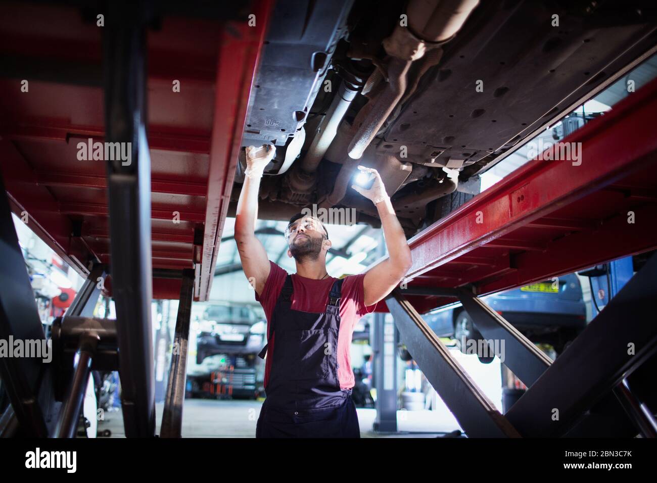 Mécanicien de sexe masculin avec lampe de poche travaillant sous une voiture dans un atelier de réparation automobile Banque D'Images