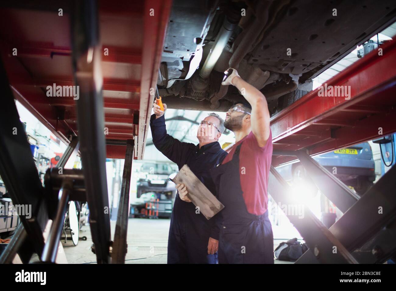 Mécanique masculine avec lampe de poche travaillant sous la voiture dans l'atelier de réparation automobile Banque D'Images