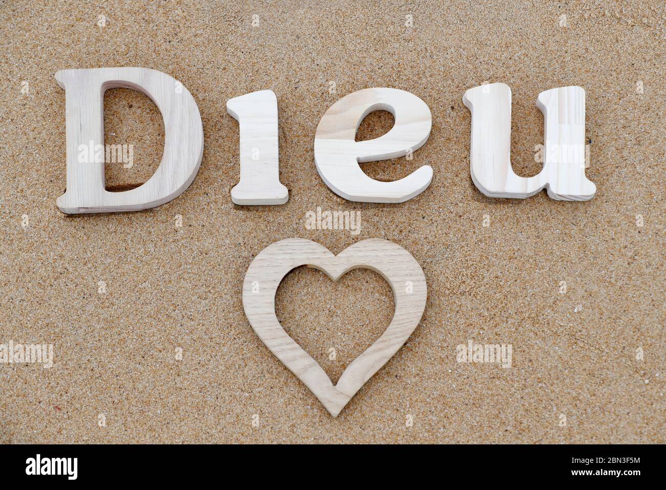 Lettres en bois formant le mot Dieu ( dieu ) avec coeur sur fond de sable de plage. Symbole chrétien. Banque D'Images