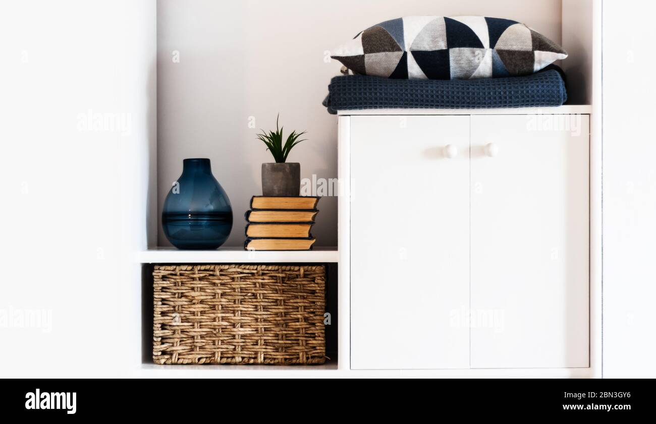 Décoration intérieure chaleureuse : oreiller, écossais, vase bleu, pile de livres, plante en pot, boîte en osier sur une étagère blanche dans la chambre. Le concept de quarantaine de s. Banque D'Images