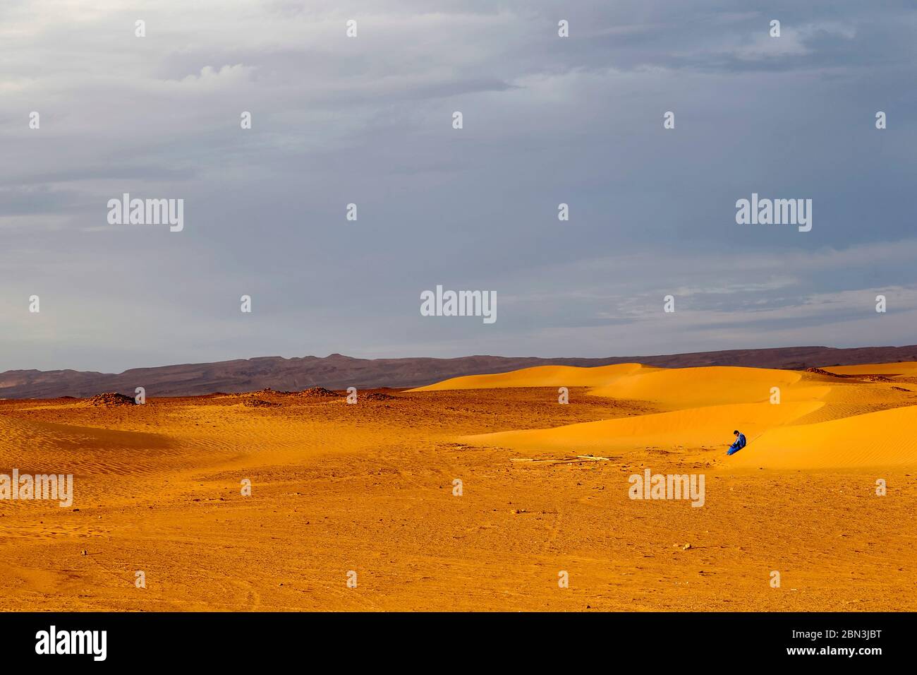 Jeune marocain assis sur une dune de sable au Sahara, Maroc. Banque D'Images