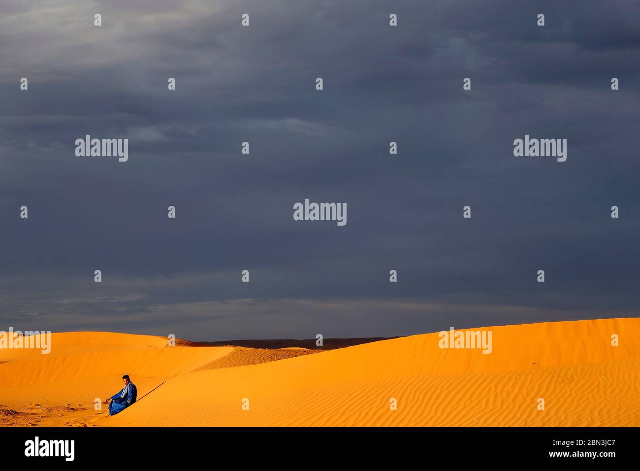 Jeune marocain assis sur une dune de sable au Sahara, Maroc. Banque D'Images