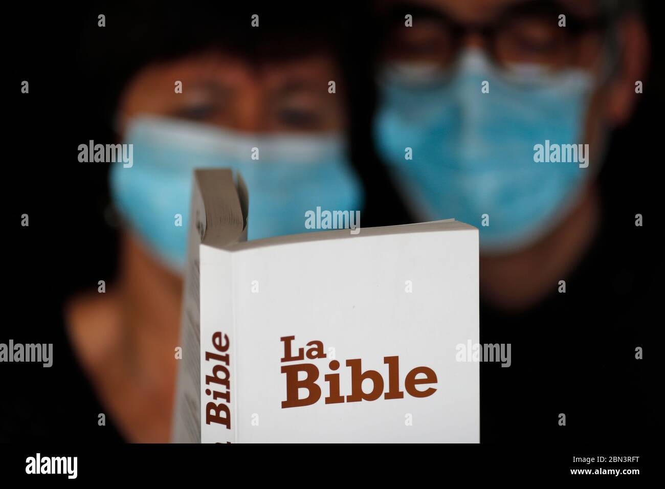 Homme et femme lisant la bible avec un masque jetable pour éviter le coronavirus contagieux ( COVID-19). France. Banque D'Images