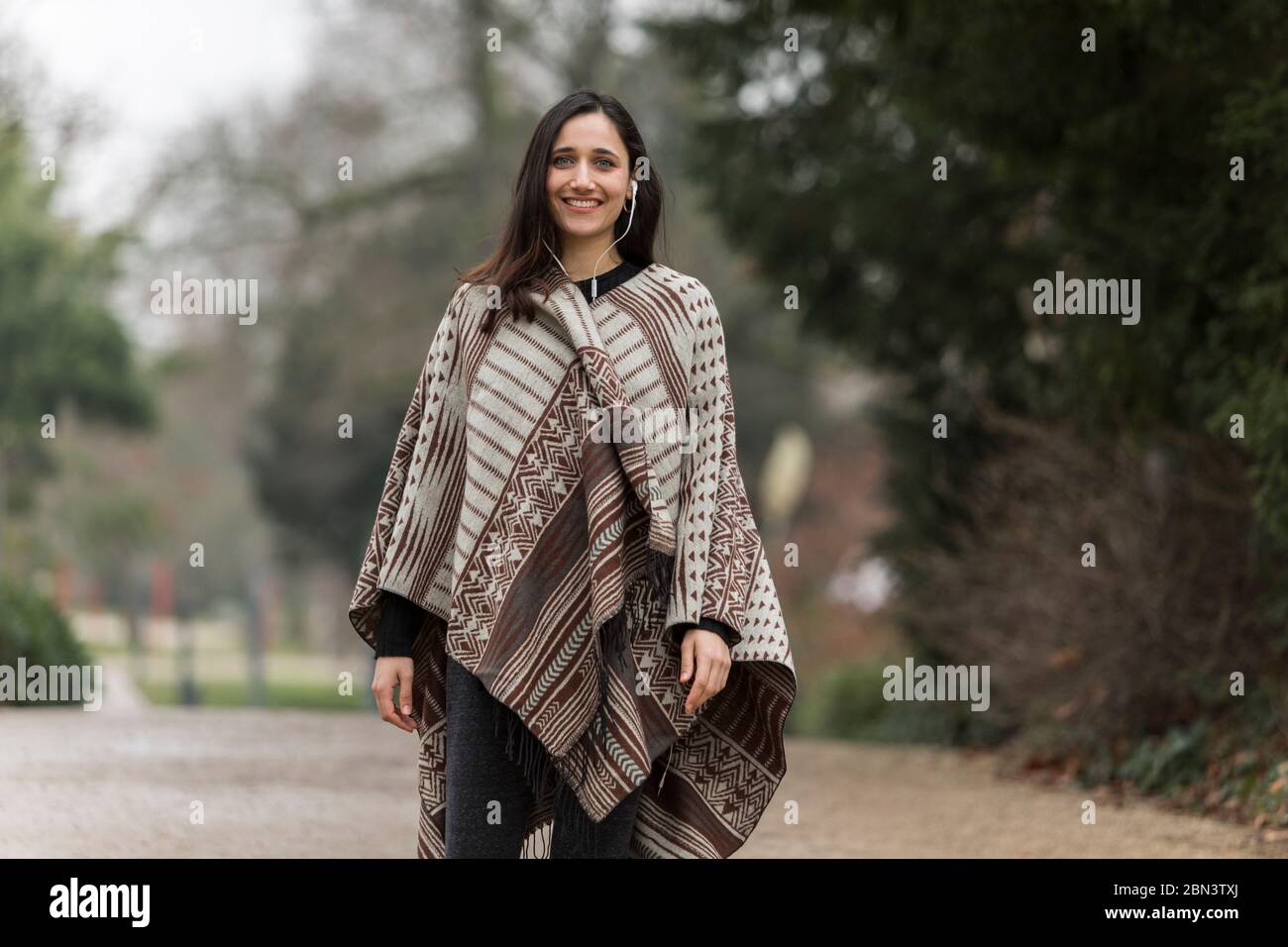 Jeune femme indienne portant un poncho souriant et souriant à l'extérieur. Banque D'Images