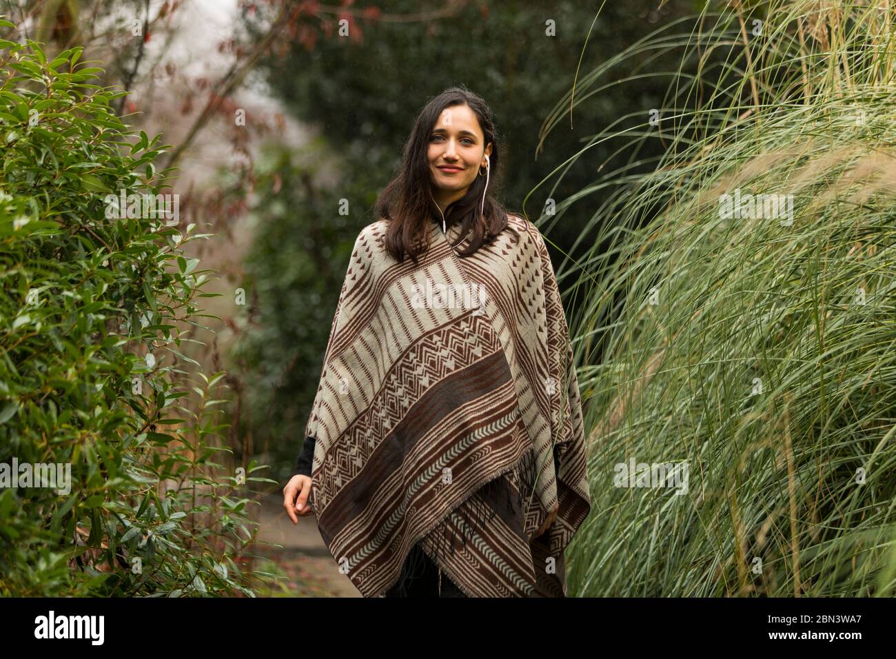 Jolie femme indienne portant un poncho posant au milieu du feuillage automnal et souriant à l'appareil photo. Banque D'Images