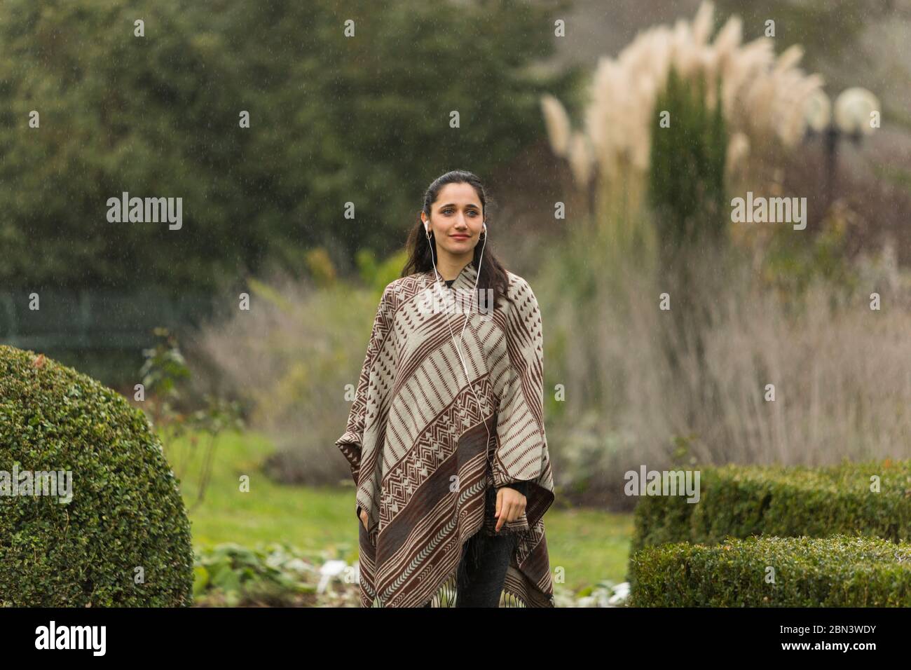 Belle femme indienne portant un poncho posé dans un jardin ornemental. Vue sur l'extérieur. Banque D'Images