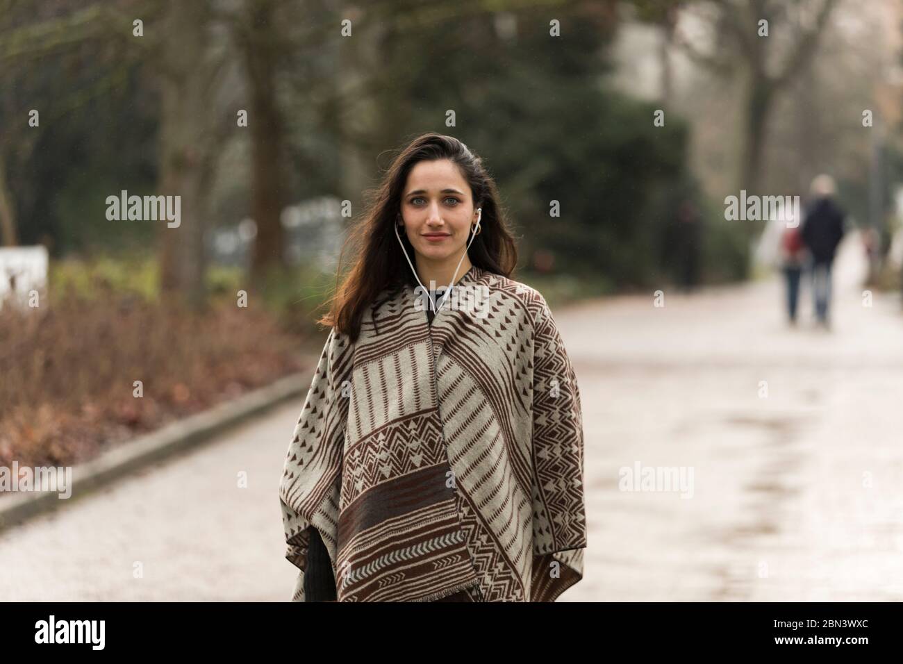 Beauté indienne portant poncho et écoutant les écouteurs posé sur la route du parc. Banque D'Images
