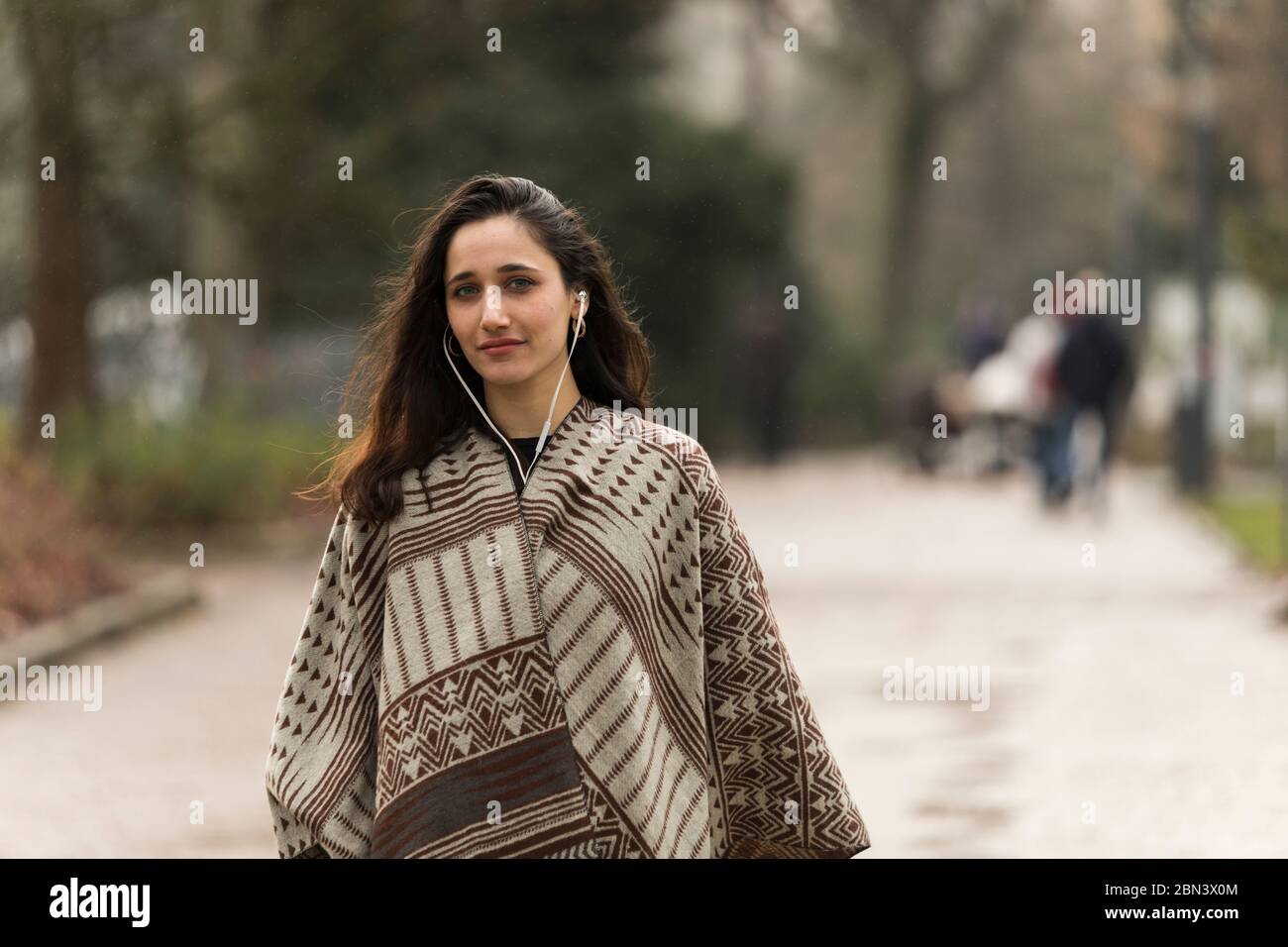 Jeune femme indienne portant un poncho et écoutant des écouteurs se posant sur la route du parc. Banque D'Images