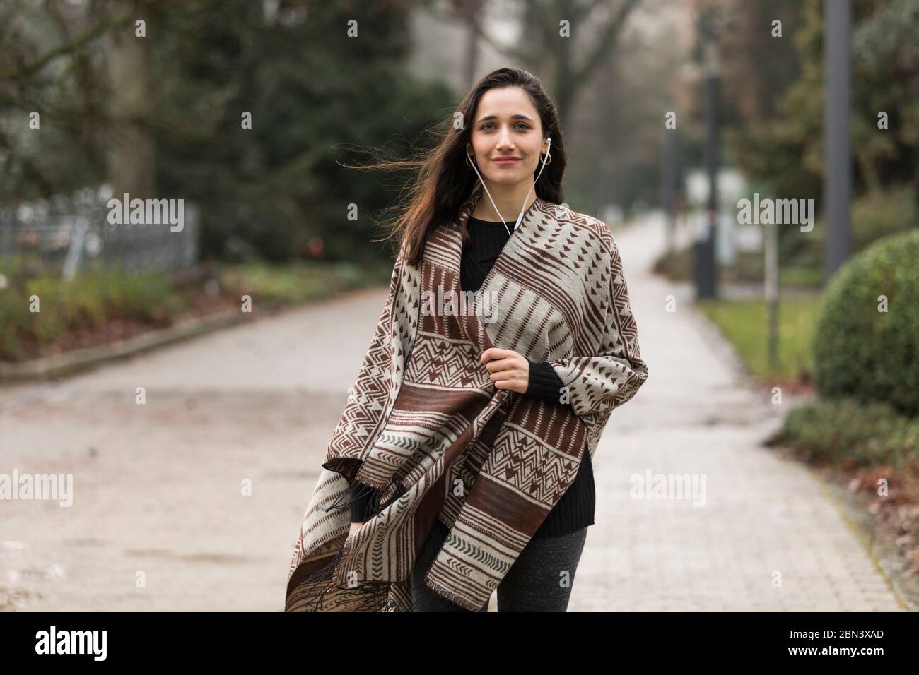 Belle femme portant un poncho et écoutant des écouteurs souriant pour l'appareil photo à l'extérieur. Banque D'Images