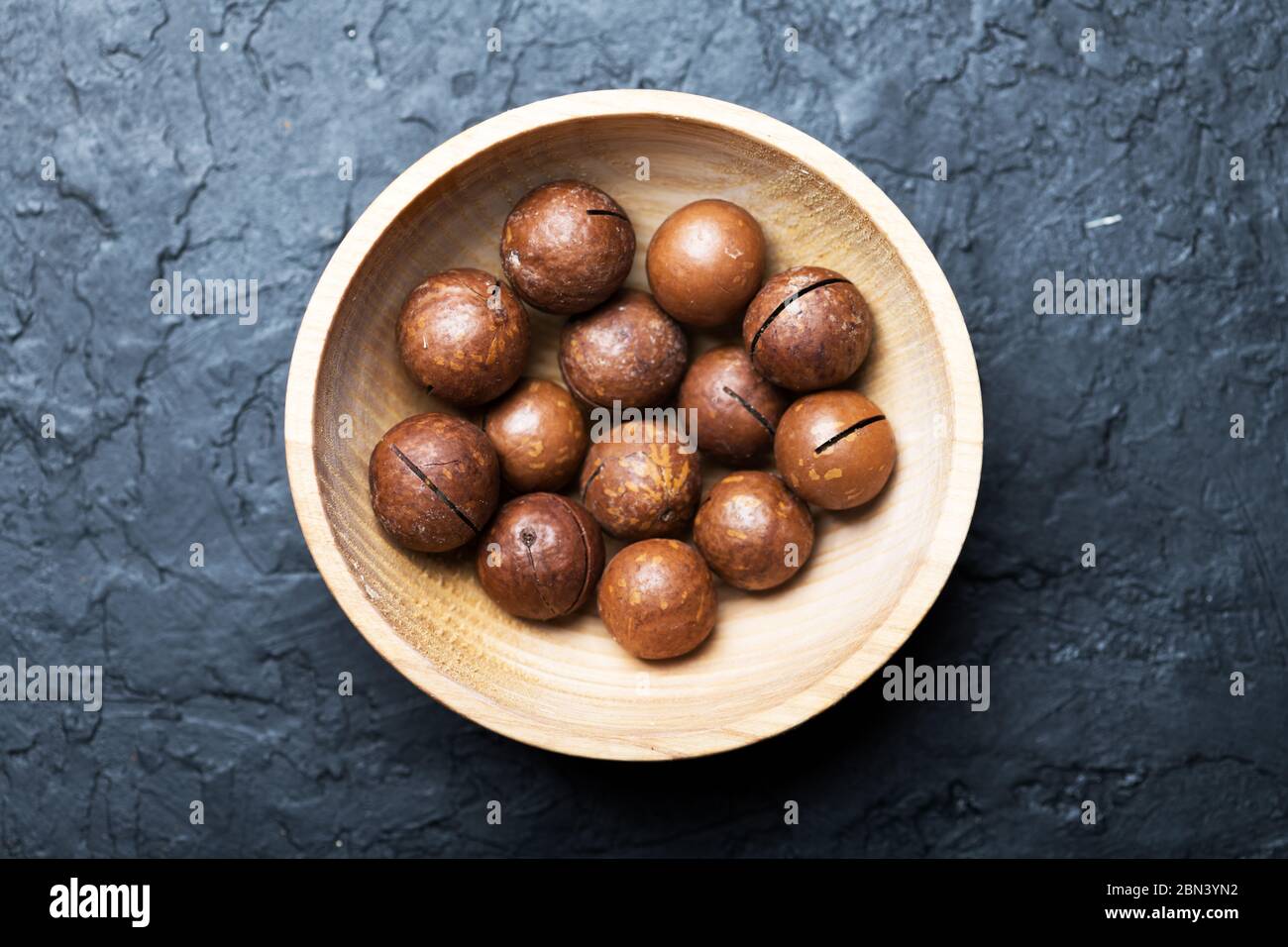 Noix de macadamia biologiques séchées dans un bol en bois. Prise de vue macro studio. Fond noir en béton Banque D'Images