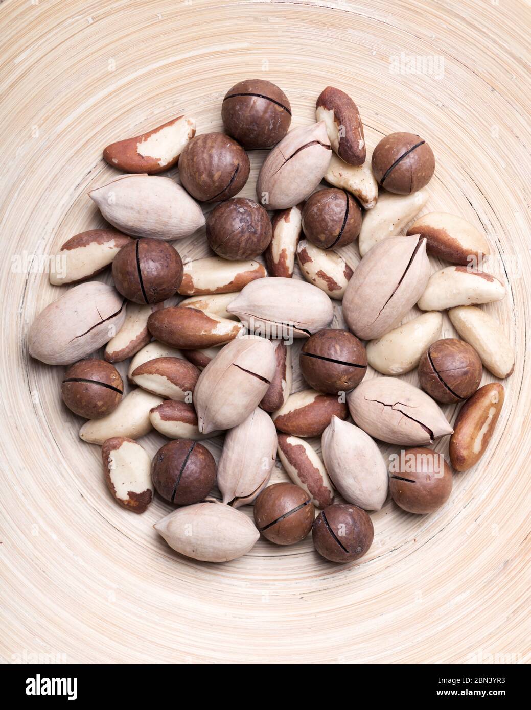 Noix mélangées séchées dans un bol en bois. Noix de macadamia, de pécan et du Brésil avec couteau sur table en bois. Prise de vue macro studio. Banque D'Images