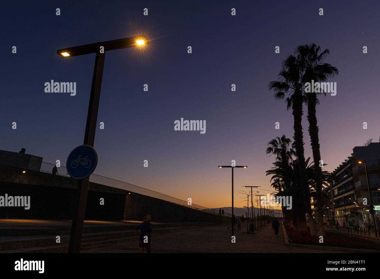 Silhoueté des gens, des lampes de rue et des palmiers au crépuscule le long du front de mer à Playa San Juan, Tenerife, îles Canaries, Espagne Banque D'Images