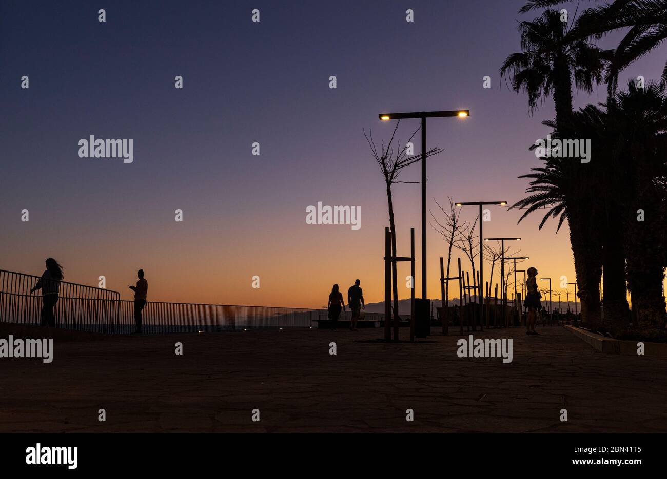 Silhoueté des gens, des lampes de rue et des palmiers au crépuscule le long du front de mer à Playa San Juan, Tenerife, îles Canaries, Espagne Banque D'Images