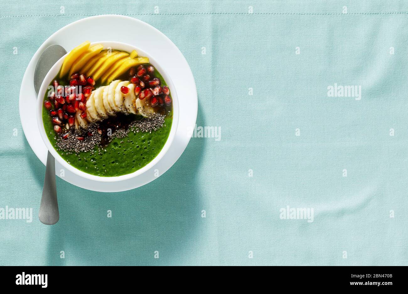 bol de smoothie vert avec des tranches de mangue, de banane, de graines de grenade et de graines de chia, sirop d'érable pour un petit déjeuner sain Banque D'Images
