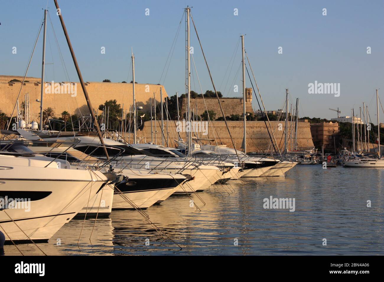Yachts à Ta' Xbiex Yacht Marina, Malte, au coucher du soleil, avec les fortifications de Floriana en arrière-plan. Voile dans la mer Méditerranée. Banque D'Images