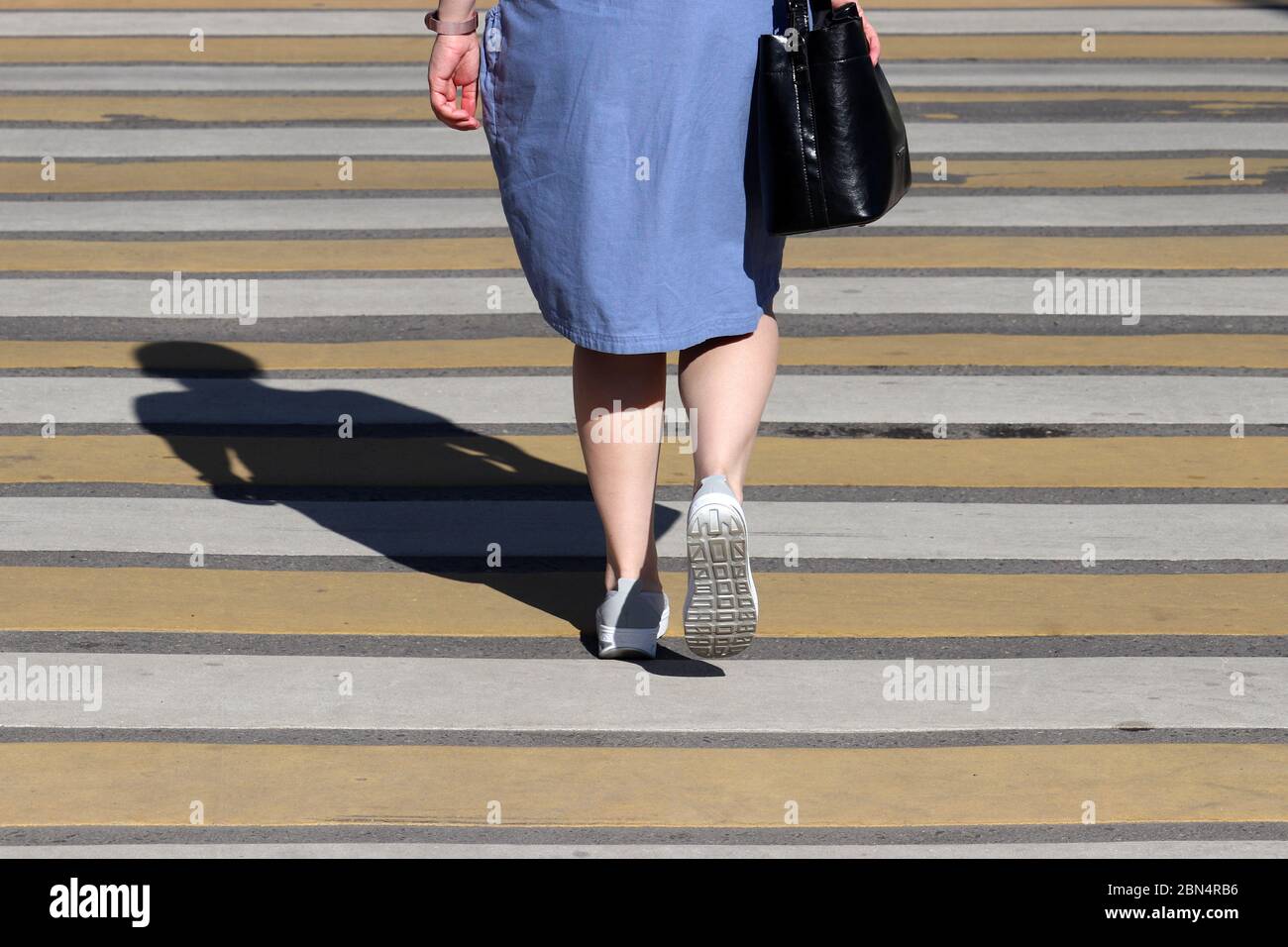 Jambes de femmes sur le passage à pied, concept de sécurité de rue. Femme dans une robe d'été marchant sur le passage de côté, ombre sur zébra Banque D'Images