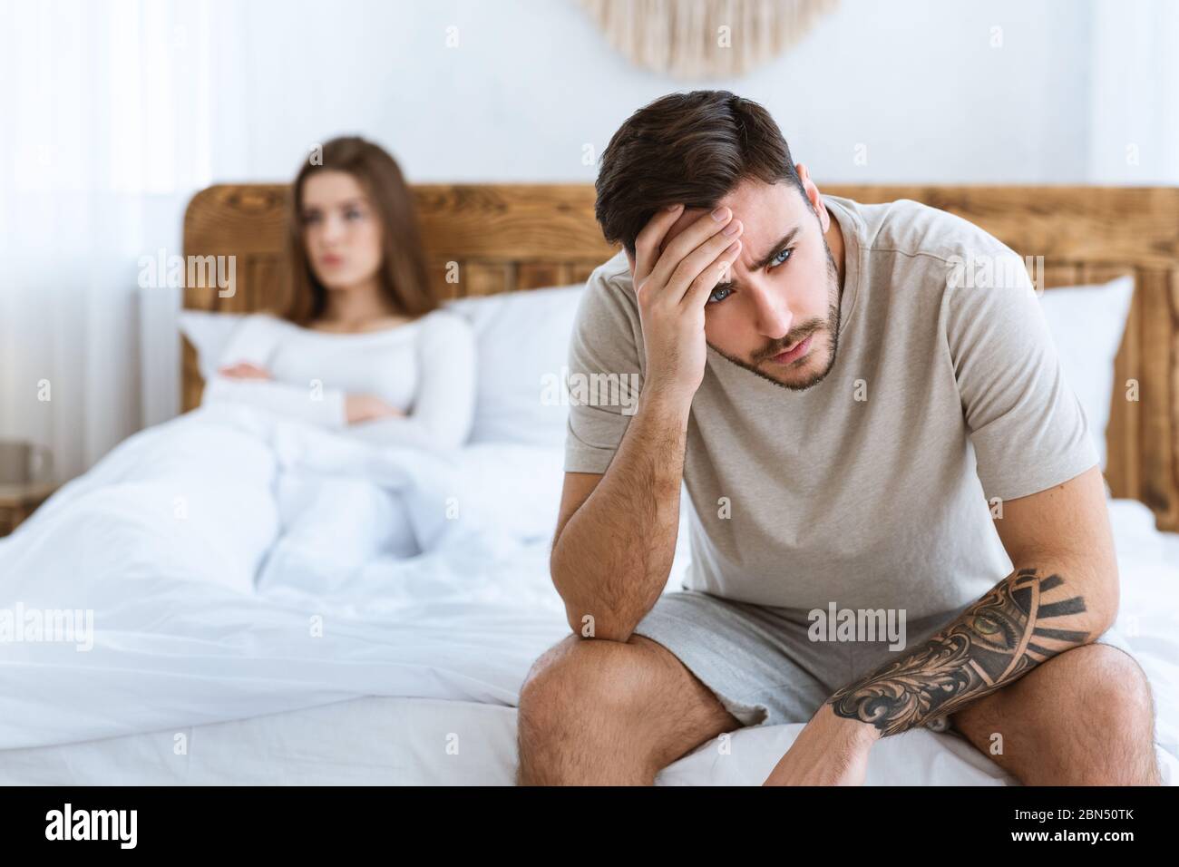 Problème au lit. L'homme s'assoit sur le lit et tient sur sa tête, la femme  est offense Photo Stock - Alamy