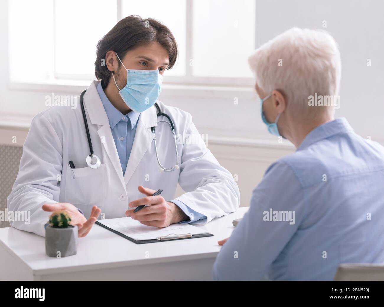 Gériatrique en masque médical parlant avec un patient âgé au bureau Banque D'Images