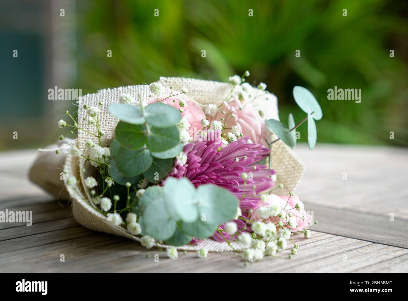 Le bouquet de fleurs à la main se compose de chrysanthème, de roses et de feuilles vertes. Sur la table. Banque D'Images