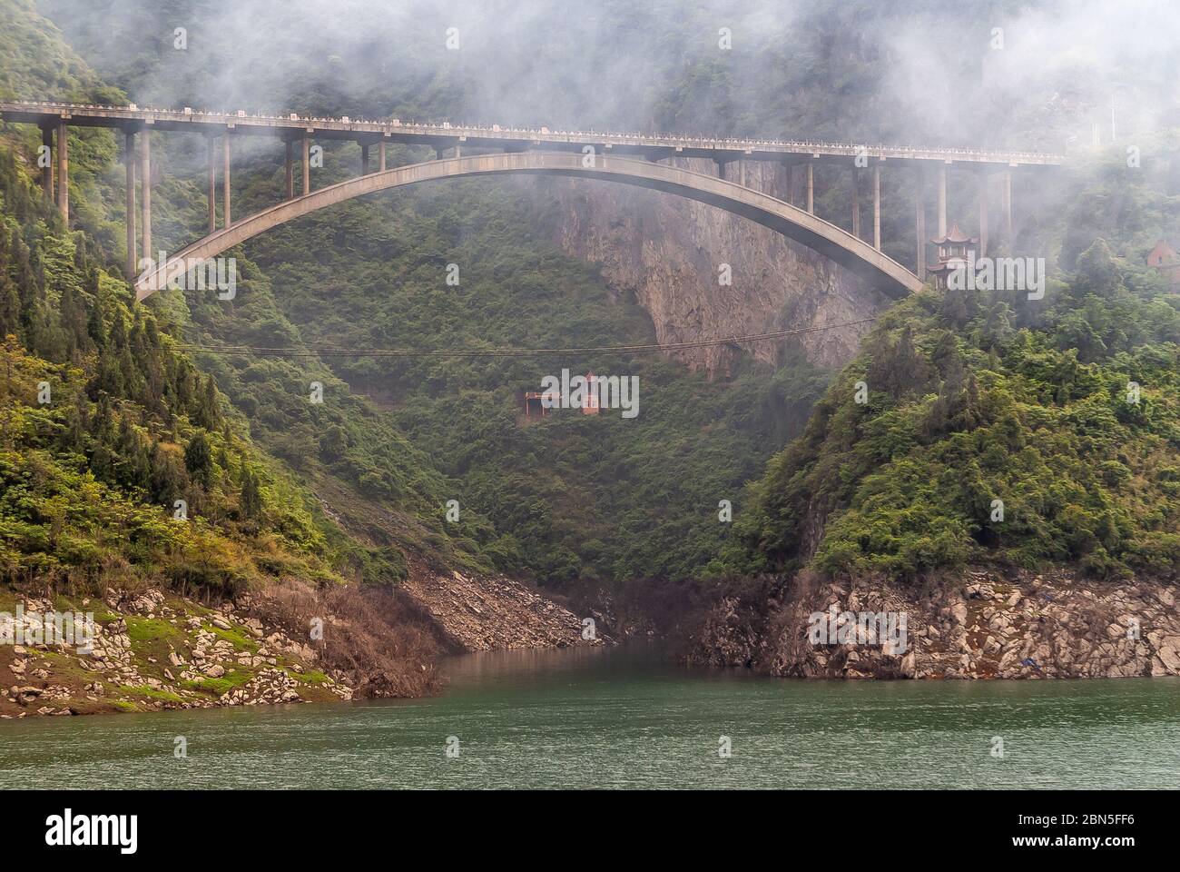 Xinling, Chine - 6 mai 2010 : gorge de Xiling sur le fleuve Yangtze. Fumée sur le pont d'arbalète en ciment brun qui enjambe le canyon entre les pentes abruptes de montagne et le claf Banque D'Images