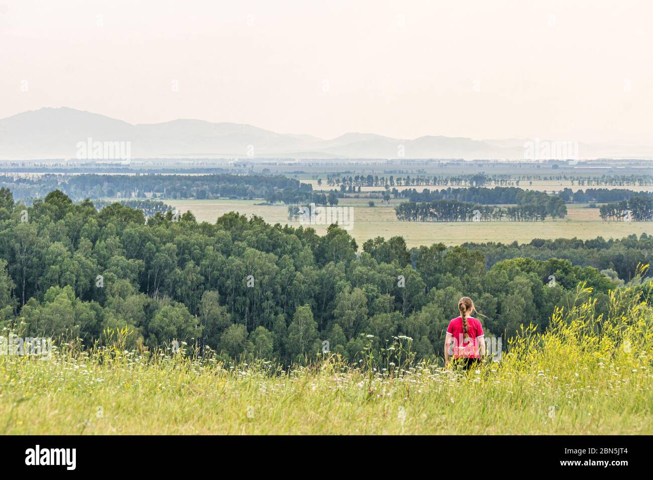 fille en rouge descend d'une colline étendues de prairies et de forêts les montagnes sont visibles, sélectif foyer Banque D'Images