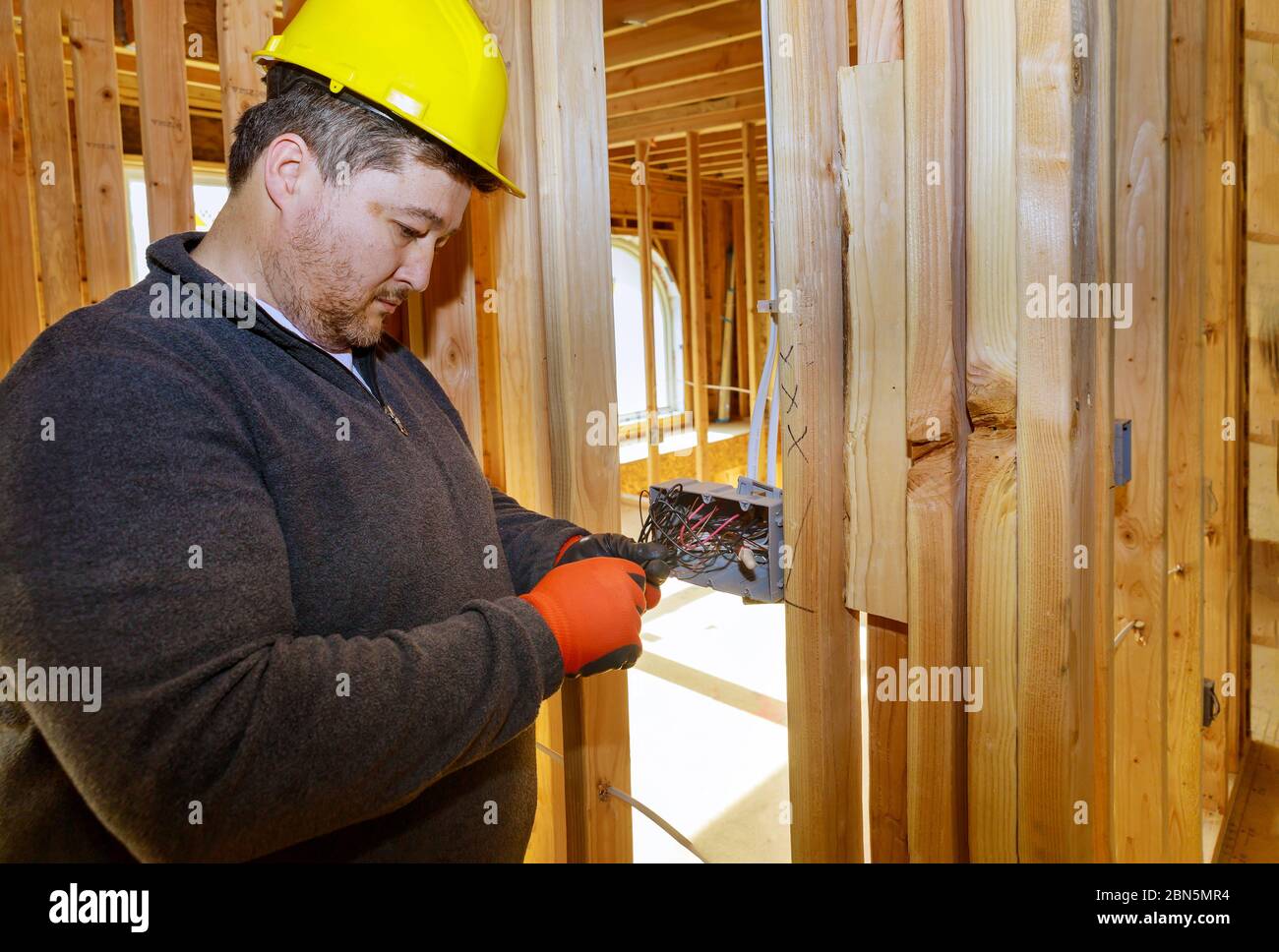 Électricien acheminant les fils dans le connecteur électrique, les prises électriques sur le mur à l'intérieur d'une maison de cadre de poutres en bois Banque D'Images