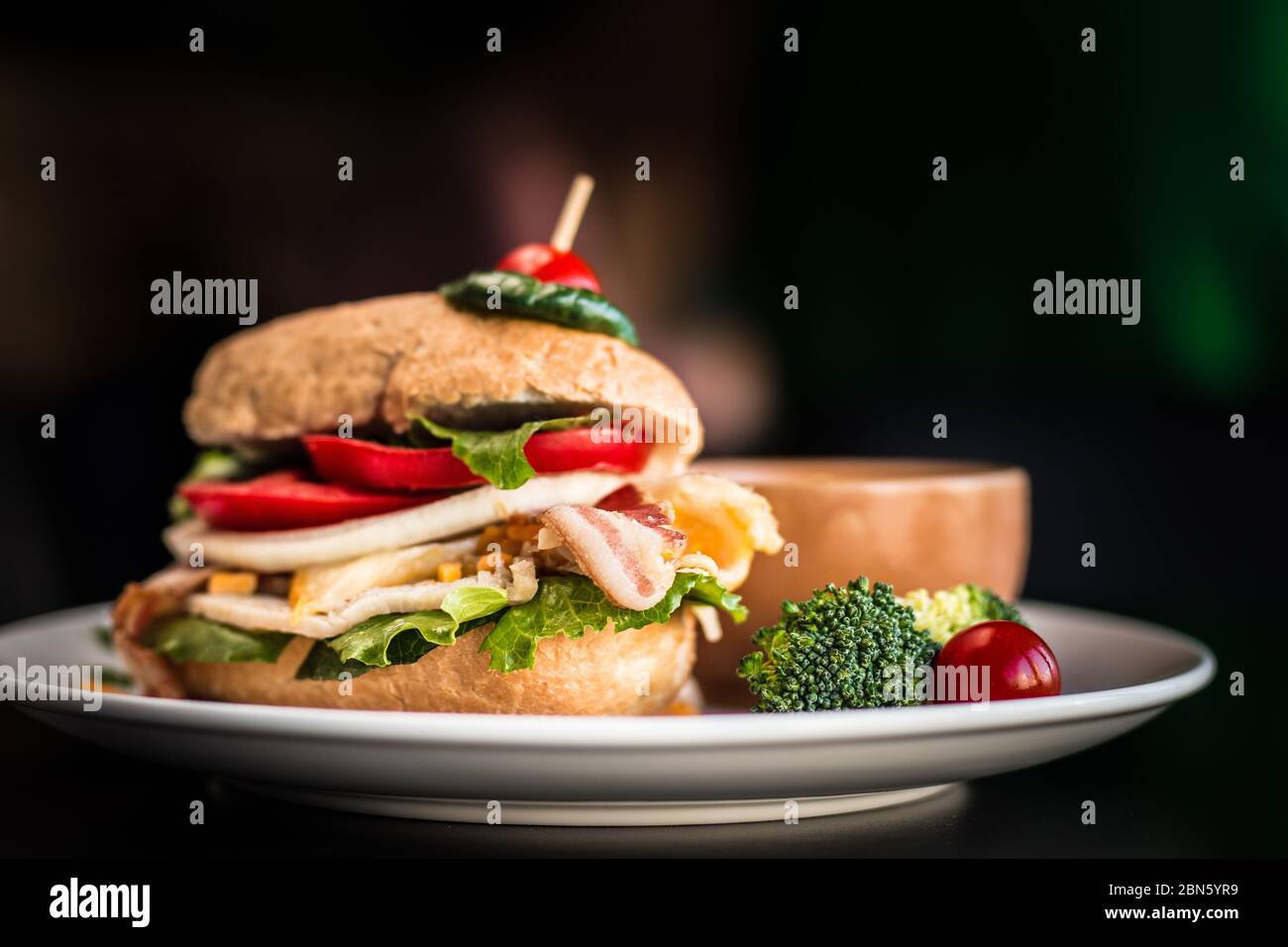 Gros plan d'un hamburger chargé avec des tomates cerises en cure-dents sur le dessus. Sandwich au bacon de légumes avec fond noir. Banque D'Images