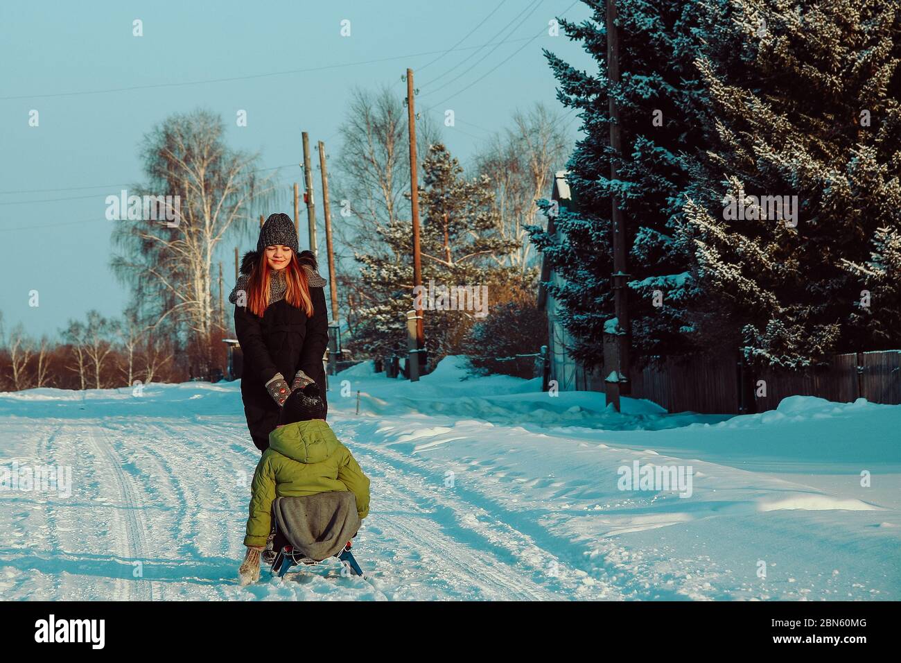 Amusement pour les enfants en hiver. Le traîneau. Une fille joue avec son frère en hiver dans la rue du village. Banque D'Images